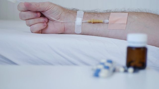 Suffering Person in Hospital with Medical Perfusion in Hand and Pills Blurred  