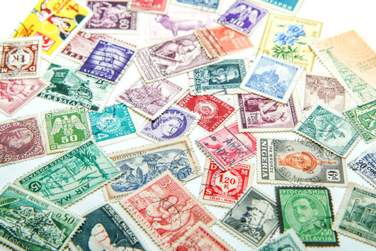 An assorted mixture of the old european and world stamps is lying on the table. Stamps are colorful and various. 