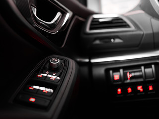 Close up controls on door and panel in black interior of modern car with red backlight
