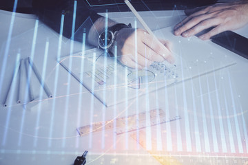 Double exposure of man's hands writing notes of stock market with forex chart.