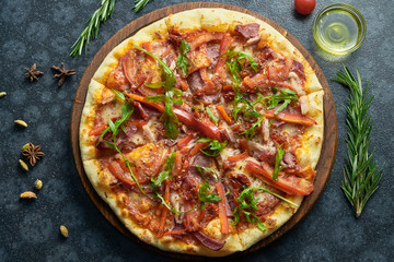 Homemade baked pizza with four kinds of meat, melted cheese, red sauce, tomatoes and ruccola on a black background in a composition with ingredients. Top view flat lay