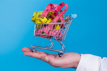 hand holding miniature supermarket cart full of tape measures, diet and slimming concept