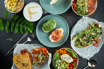 Assorted hipster street food on a dark background: avocado toasts with salmon and poached egg, coffee, Buddha bowl and sandwich with jamon. Top view, food flat lay