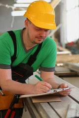 Portrait of young attractive man in work clothes and yellow helmet crossed arms smiling at shop for manufacturing furniture and details home interior