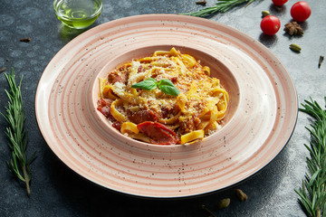 Homemade and fresh pasta bolognese with minced meat, parmesan, tomatoes and basil. Italian pasta tagliatelle in a pink ceramic plate on a black background in a composition with ingredients