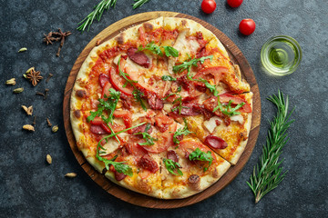 Homemade baked pizza with tomatoes, arugula, red sauce, salami and hunting sausages on a black background in a composition with ingredients. Top view flat lay