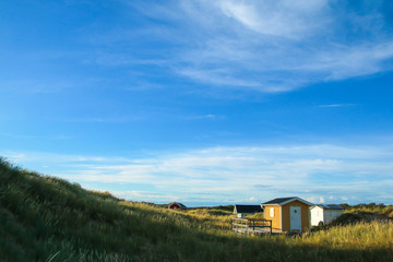 Fototapeta na wymiar The traditional colorful wooden recreational cottages by the coast of the sea in Sweden, hidden behind the dunes.