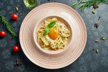 Homemade and fresh carbonara pasta with yolk and parmesan. Italian appetizing spaghetti in a pink plate on a black background in a composition with ingredients