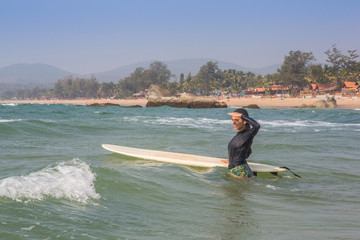 A girl in the ocean looking out for waves as she stands next to her surfboard.