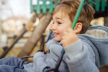 Portrait of a small little cute caucasian boy three years old having fun smiling on the swing in the park in winter or autumn day wearing coat