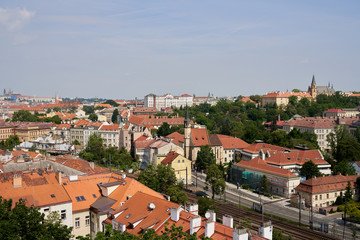 Fototapeta na wymiar Typical roofs. Top view - roofs with red tiles in old buildings. There are beautiful houses in green trees. Horizontal photo colorful European city Prague in Czech Republic, travel in tourist place
