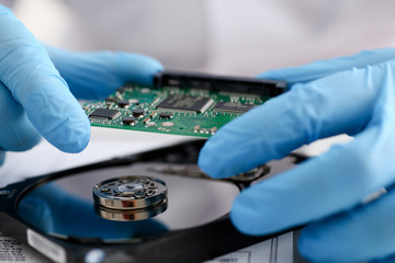 A male repairman wearing blue gloves is holding a hard drive from computer or laptop in hands....