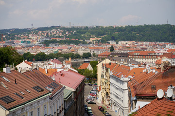 Typical roofs. Top view - roofs with red tiles in old buildings. There are beautiful houses in green trees. Horizontal photo colorful European city Prague in Czech Republic, travel in tourist place