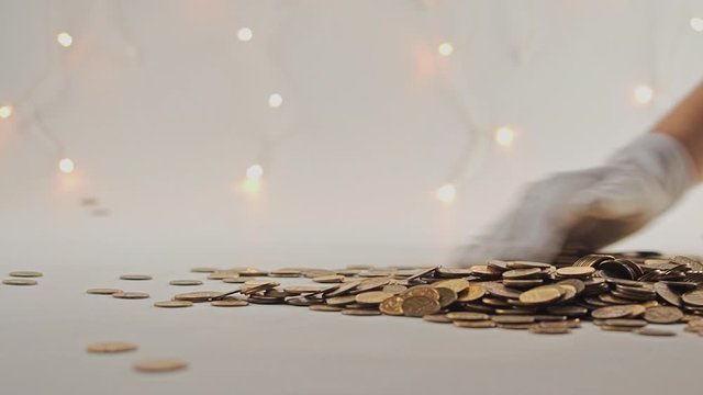 White-gloved hands scooping up a pile of gold coins. They sort out and scatter money.On white background. Garland. Money glitters.