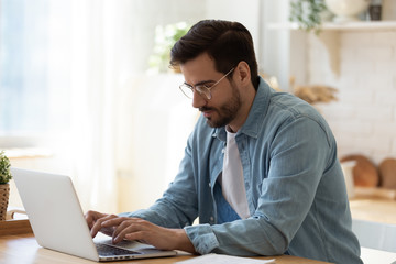 Handsome young businessman in eyewear working with computer remotely.