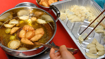 lady deep frying traditional Chinese Yau Kok Zai or sweet dumpling with some raw ones nearby for Chinese New Year
