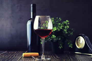 A glass of red dry wine on the table. Dark bottle and glass of wine.