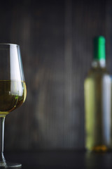 Transparent bottle of white dry wine on the table. White wine glass on a wooden background.