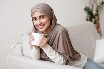 Muslim girl in hijab relaxing at home with cup of coffee