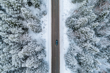 Aerial view of winter road with a car and snow covered forest in Finland