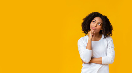 Doubtful afro girl thinking about something over yellow background - obrazy, fototapety, plakaty