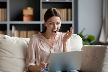 Excited millennial girl shocked by news on laptop