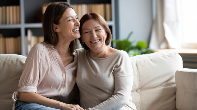 Happy senior mother and adult daughter laugh relaxing at home