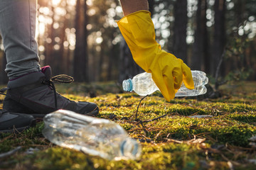 Hand in protective glove picking up plastic bottle in forest - obrazy, fototapety, plakaty