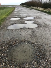 picture with dirty and bumpy country road, reflections in water puddles