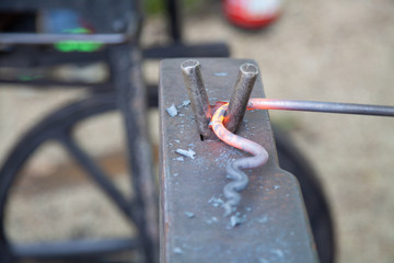 Glowing iron is deformed and forged on the subscription with a mobile chimney in the background.