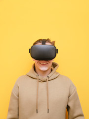 Portrait of happy young man in vr helmet on yellow background, looking into camera and smiling. Guy is playing VR games. Cheerful teenager with VR helmet isolated on yellow background. vertical