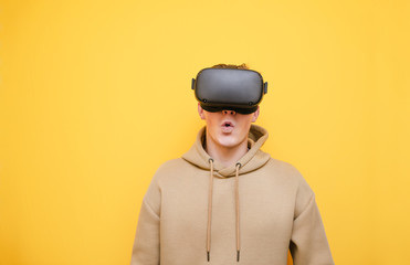 Portrait of emotionally young man in VR helmet isolated on yellow background, looking into camera with surprised face. Shocked guy in VR helmet stands on yellow background. Realistic VR gaming.