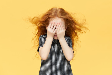 Isolated shot of timid little girl being shy, covering eyes. Red haired female child hiding tears...