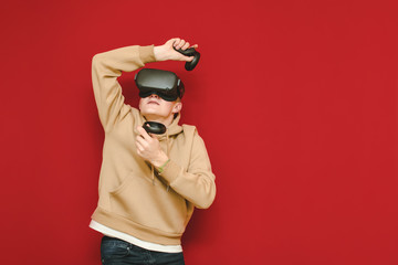 Young man in VR helmet stands on red background, looks up with surprised face. Portrait of frightened guy in virtual reality helmet playing games in virtual reality