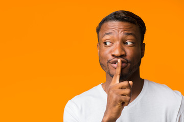 Fototapeta na wymiar Afro Guy Gesturing Finger On Lips Standing Over Orange Background