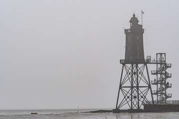 Fototapeta na wymiar old lighthouse with low tide and fog at the northsea