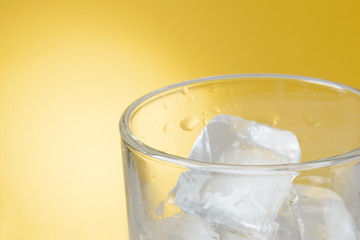 part of a glass of cold water with ice on a yellow background