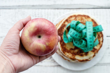 hand holding a red Apple on a background of pancakes with a centimeter tape. the concept of a...