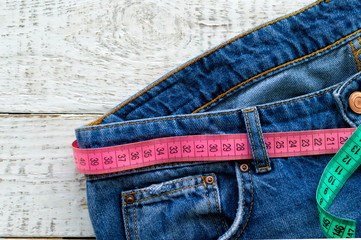 Top of denim trousers, on a wooden background. Blue jeans with a measuring tape instead of a belt. jeans with a measuring tape around the waist. The concept of a healthy lifestyle and diet.