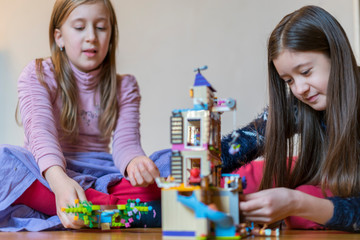 Fototapeta premium Two little sisters are playing children's constructor at home. selected focus