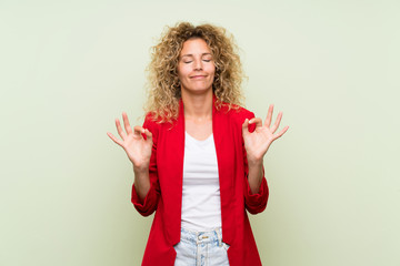 Young blonde woman with curly hair over isolated green background in zen pose