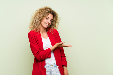 Fototapeta na wymiar Young blonde woman with curly hair over isolated green background presenting an idea while looking smiling towards