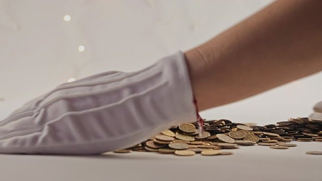 White-gloved hands scooping up a pile of gold coins. They sort out and scatter money.On white background. Garland. Money glitters.