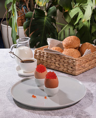 Breakfast. Chicken eggs stuffed with red caviar on stands, fresh sesame buns, freshly brewed coffee and a pitcher of cream.