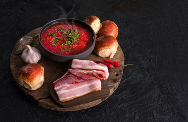 Traditional Ukrainian or Russian red vegetable and meat soup borscht in a cast-iron pot with garlic buns and sour cream on a black background. Traditional Slavic dish. copy space.