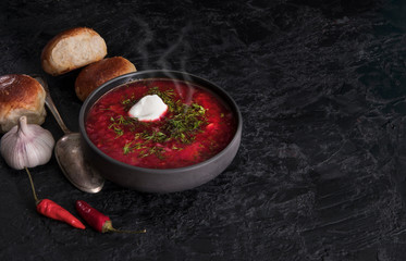 Traditional Ukrainian or Russian red vegetable and meat soup borscht in a cast-iron pot with garlic buns and sour cream on a black background. Traditional Slavic dish. copy space.