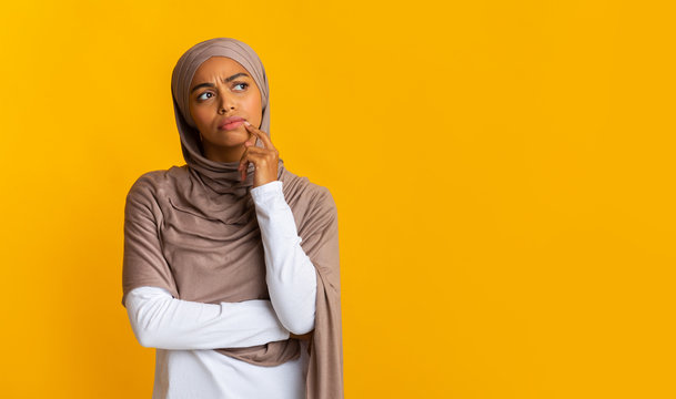 Portrait of doubtful afro islamic girl in headscarf over yellow background