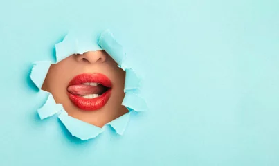 Woman with red lips playing with tongue in turquoise paper hole © Prostock-studio