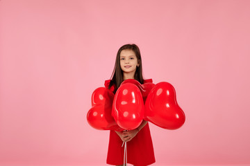 valentine's day. smiling child girl holding red heart shaped balloon isolated on pink background. copy space