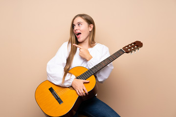 Fototapeta premium Teenager girl with guitar over isolated background surprised and pointing side
